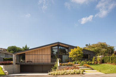 Large midcentury two-storey black exterior in Seattle with a gable roof and mixed siding.