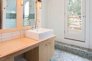 Alcove shower - mid-sized contemporary white tile and ceramic tile pebble tile floor alcove shower idea in Minneapolis with a vessel sink, flat-panel cabinets, light wood cabinets, white walls and wood countertops