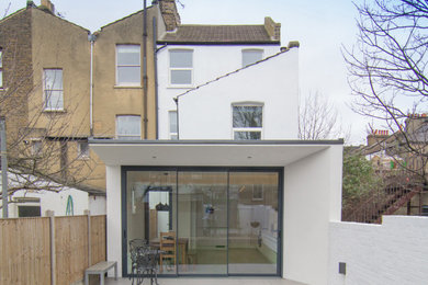 Photo of a medium sized and white render and rear house exterior in London with three floors, a flat roof and a grey roof.