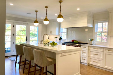 Minimalist light wood floor and beige floor eat-in kitchen photo in Chicago with a farmhouse sink, recessed-panel cabinets, white cabinets, solid surface countertops, white backsplash, ceramic backsplash, an island and white countertops