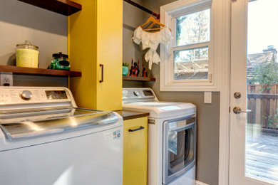 Small eclectic porcelain tile and black floor laundry room photo in San Francisco with flat-panel cabinets, yellow cabinets, wood countertops, gray walls and a side-by-side washer/dryer
