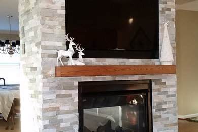 Mid-sized trendy open concept medium tone wood floor living room photo in Other with beige walls, a two-sided fireplace, a stone fireplace and a wall-mounted tv