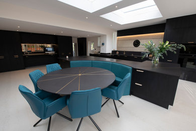This is an example of an expansive modern cream and black kitchen/diner in Kent with a submerged sink, flat-panel cabinets, black cabinets, engineered stone countertops, black appliances, porcelain flooring, an island and black worktops.
