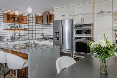 Mid-sized trendy l-shaped vinyl floor and gray floor open concept kitchen photo in San Diego with an undermount sink, flat-panel cabinets, white cabinets, glass countertops, multicolored backsplash, subway tile backsplash, stainless steel appliances, an island and gray countertops