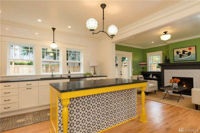 Mid-sized transitional l-shaped light wood floor eat-in kitchen photo in Seattle with a drop-in sink, shaker cabinets, white cabinets, granite countertops, white backsplash, subway tile backsplash, stainless steel appliances, an island and black countertops
