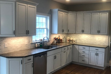 This is an example of a large modern u-shaped eat-in kitchen in New York with an undermount sink, raised-panel cabinets, white cabinets, quartzite benchtops, grey splashback, marble splashback, stainless steel appliances, medium hardwood floors, with island, brown floor and black benchtop.