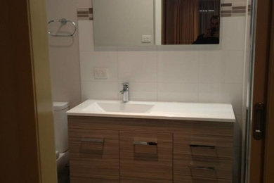 This is an example of a small modern 3/4 bathroom in Other with beaded inset cabinets, brown cabinets, an alcove shower, a two-piece toilet, white tile, ceramic tile, white walls, porcelain floors, an integrated sink and solid surface benchtops.