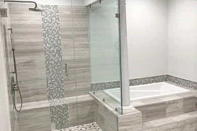 Traditional master bathroom with a drop-in tub, a corner shower, gray tile, limestone, grey walls, porcelain floors, grey floor and a hinged shower door.