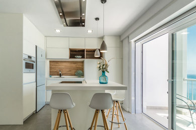 Cette image montre une cuisine américaine méditerranéenne en L de taille moyenne avec un évier posé, un placard à porte plane, des portes de placard blanches, une crédence beige, une crédence en bois, un électroménager blanc, un sol en carrelage de céramique, îlot, un sol gris et un plan de travail blanc.