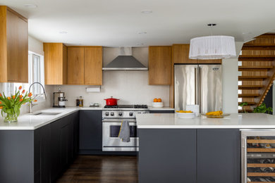 Small 1950s l-shaped dark wood floor and brown floor open concept kitchen photo in New York with an undermount sink, flat-panel cabinets, black cabinets, quartz countertops, white backsplash, ceramic backsplash, stainless steel appliances, an island and white countertops
