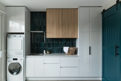 Photo of a medium sized contemporary utility room in Melbourne with a single-bowl sink, open cabinets, light wood cabinets, glass worktops, blue splashback, cement tile splashback, white walls, concrete flooring, a stacked washer and dryer, grey floors and grey worktops.