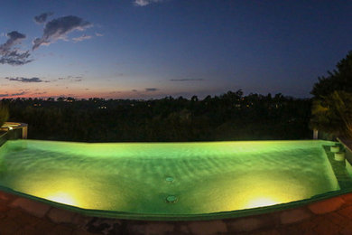 Foto de piscina infinita mediterránea grande rectangular en patio trasero con adoquines de piedra natural