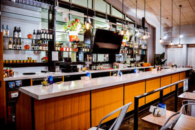 Seated home bar - large galley porcelain tile and brown floor seated home bar idea in Seattle with no sink, flat-panel cabinets, light wood cabinets, quartz countertops, white backsplash, quartz backsplash and white countertops