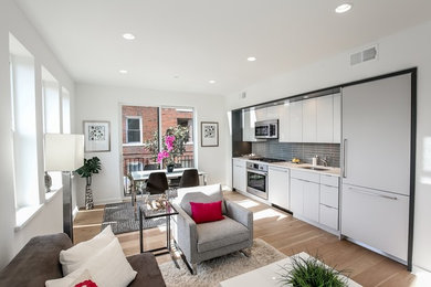 Example of a small minimalist single-wall light wood floor eat-in kitchen design in DC Metro with a drop-in sink, flat-panel cabinets, white cabinets, quartz countertops, gray backsplash, ceramic backsplash, paneled appliances and an island
