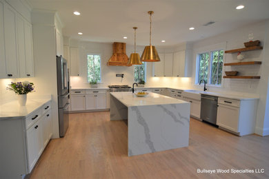 Design ideas for a large traditional u-shaped open plan kitchen in DC Metro with a belfast sink, shaker cabinets, white cabinets, engineered stone countertops, white splashback, ceramic splashback, stainless steel appliances, light hardwood flooring, an island, brown floors and white worktops.