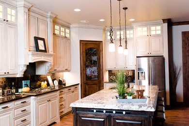 Example of a large classic l-shaped light wood floor and brown floor kitchen design in Oklahoma City with an undermount sink, raised-panel cabinets, white cabinets, granite countertops, stone slab backsplash, stainless steel appliances and an island