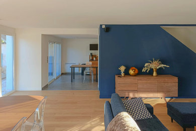 Aménagement d'un grand salon blanc et bois contemporain ouvert avec une salle de réception, un mur bleu, parquet clair, un poêle à bois, un téléviseur encastré et un sol beige.