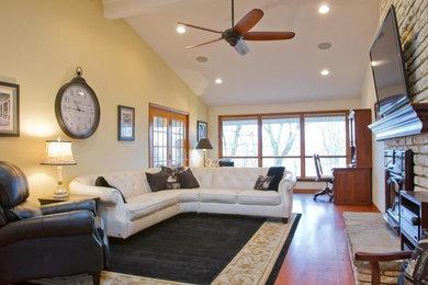 Mid-sized elegant open concept medium tone wood floor and brown floor family room photo in Columbus with beige walls, a standard fireplace, a stone fireplace and a wall-mounted tv