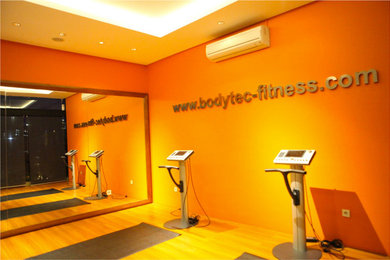 Idee per uno studio yoga industriale di medie dimensioni con pareti arancioni, pavimento in laminato e pavimento marrone