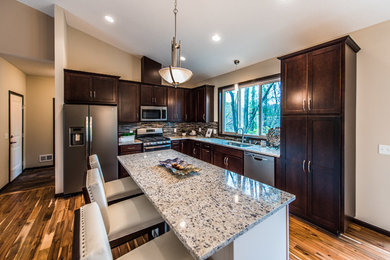 Eat-in kitchen - mid-sized transitional l-shaped brown floor and medium tone wood floor eat-in kitchen idea in Minneapolis with an undermount sink, shaker cabinets, dark wood cabinets, granite countertops, multicolored backsplash, matchstick tile backsplash, stainless steel appliances and an island