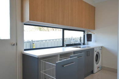 Design ideas for a mid-sized modern l-shaped dedicated laundry room in Adelaide with light wood cabinets, laminate benchtops, white walls and porcelain floors.