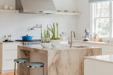 Photo of a beach style u-shaped kitchen in Boston with an undermount sink, flat-panel cabinets, white cabinets, marble benchtops, white splashback, stainless steel appliances, medium hardwood floors, with island and brown floor.