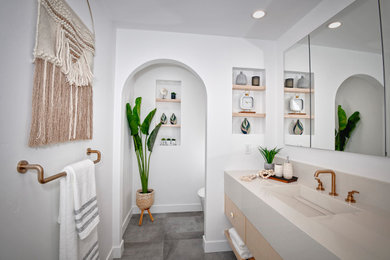 Inspiration for a large contemporary ensuite bathroom in San Diego with flat-panel cabinets, light wood cabinets, a freestanding bath, a walk-in shower, a bidet, grey tiles, porcelain tiles, white walls, pebble tile flooring, an integrated sink, engineered stone worktops, multi-coloured floors, an open shower, beige worktops, a wall niche, a single sink and a floating vanity unit.