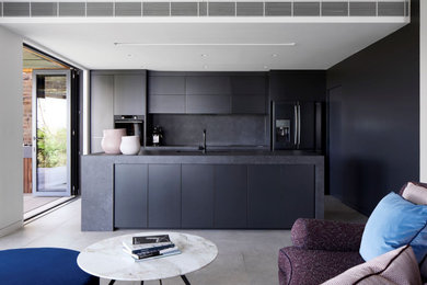 This is an example of a mid-sized contemporary galley open plan kitchen in Sydney with an undermount sink, grey cabinets, grey splashback, stone slab splashback, black appliances, cement tiles, with island, grey floor, grey benchtop and solid surface benchtops.