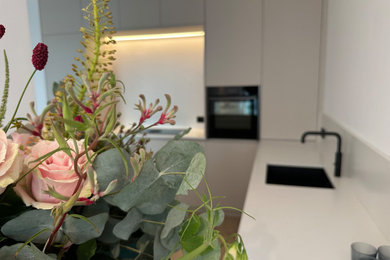 Offene, Große Moderne Küche in U-Form mit Unterbauwaschbecken, flächenbündigen Schrankfronten, Mineralwerkstoff-Arbeitsplatte, schwarzen Elektrogeräten und hellem Holzboden in Düsseldorf