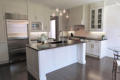 Large trendy l-shaped dark wood floor eat-in kitchen photo in Toronto with an undermount sink, shaker cabinets, white cabinets, soapstone countertops, white backsplash, stone tile backsplash, stainless steel appliances and an island