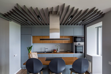 Photo of a mid-sized contemporary galley eat-in kitchen in Moscow with a drop-in sink, flat-panel cabinets, blue cabinets, grey splashback, stainless steel appliances and with island.