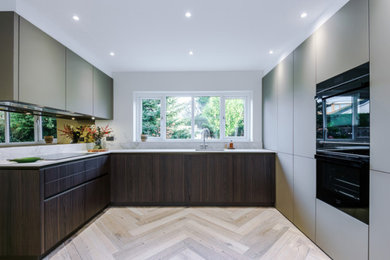 This is an example of a large contemporary open plan kitchen in Manchester with an integrated sink, flat-panel cabinets, metallic splashback, mirror splashback, stainless steel appliances, porcelain flooring, an island, beige floors and beige worktops.
