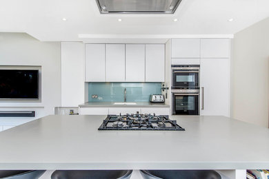 Photo of a contemporary single-wall kitchen in Other with a submerged sink, flat-panel cabinets, white cabinets, blue splashback, glass sheet splashback, integrated appliances and an island.