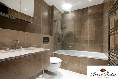 Design ideas for a medium sized contemporary ensuite bathroom in London with a wall-mounted sink, glass-front cabinets, light wood cabinets, marble worktops, a built-in bath, a shower/bath combination, a wall mounted toilet, beige tiles, stone tiles and marble flooring.