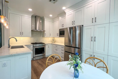 Example of a mid-sized trendy u-shaped laminate floor and brown floor eat-in kitchen design in San Diego with an undermount sink, shaker cabinets, white cabinets, quartz countertops, white backsplash, quartz backsplash, stainless steel appliances, a peninsula and white countertops