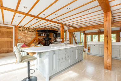 Photo of an expansive farmhouse galley open plan kitchen in Hertfordshire with an integrated sink, shaker cabinets, blue cabinets, engineered stone countertops, white splashback, engineered quartz splashback, coloured appliances, terracotta flooring, an island, beige floors, white worktops, exposed beams and a feature wall.