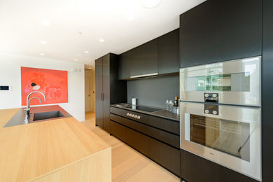 Inspiration for a mid-sized modern single-wall light wood floor open concept kitchen remodel in Vancouver with an integrated sink, flat-panel cabinets, black cabinets, black backsplash and an island