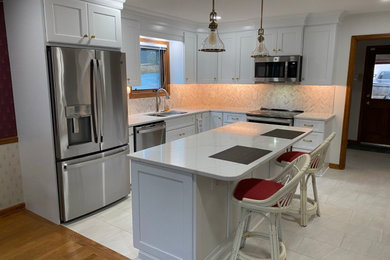 Example of a mid-sized arts and crafts l-shaped vinyl floor and multicolored floor eat-in kitchen design in Atlanta with an undermount sink, shaker cabinets, white cabinets, quartz countertops, white backsplash, marble backsplash, stainless steel appliances, an island and white countertops