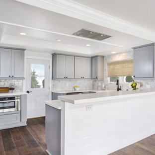 Small traditional kitchen pantry remodeling - Example of a small classic u-shaped medium tone wood floor kitchen pantry design in Orange County with a farmhouse sink, shaker cabinets, quartz countertops, multicolored backsplash, stone tile backsplash, stainless steel appliances and a peninsula