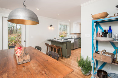 Eat-in kitchen - mid-sized transitional l-shaped light wood floor eat-in kitchen idea in Boston with a farmhouse sink, recessed-panel cabinets, green cabinets, soapstone countertops, white backsplash, subway tile backsplash, stainless steel appliances and a peninsula