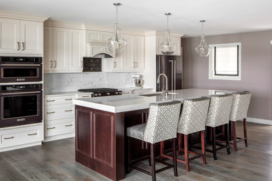 Example of a classic medium tone wood floor kitchen design in Other with quartz countertops, an undermount sink, shaker cabinets, beige cabinets, white backsplash, stainless steel appliances, an island and gray countertops