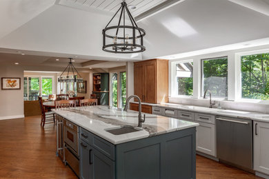 Inspiration for a large transitional u-shaped medium tone wood floor, brown floor and tray ceiling eat-in kitchen remodel in Columbus with an undermount sink, shaker cabinets, quartz countertops, white backsplash, ceramic backsplash, stainless steel appliances, an island and white countertops