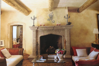 Cette photo montre un grand salon méditerranéen ouvert avec un mur beige, tomettes au sol, une cheminée standard, un manteau de cheminée en pierre, un sol beige et poutres apparentes.