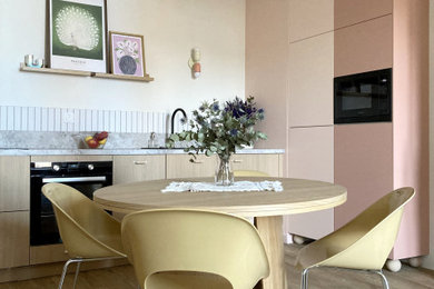 Exemple d'une cuisine ouverte linéaire, encastrable et bicolore tendance de taille moyenne avec un évier 1 bac, un placard à porte affleurante, des portes de placard rose, un plan de travail en granite, une crédence blanche, une crédence en céramique, sol en stratifié, un sol marron et un plan de travail gris.