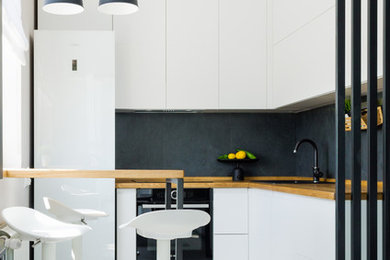 Design ideas for a small contemporary l-shaped open plan kitchen in Other with flat-panel cabinets, white cabinets, wood benchtops, black splashback, porcelain splashback, white floor, a drop-in sink, black appliances and brown benchtop.