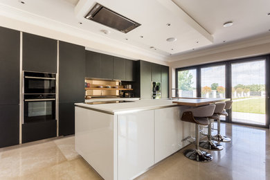 This is an example of a mid-sized contemporary single-wall kitchen in Hertfordshire with flat-panel cabinets, quartzite benchtops, with island, beige floor, white benchtop, an undermount sink, black cabinets, black appliances and metallic splashback.