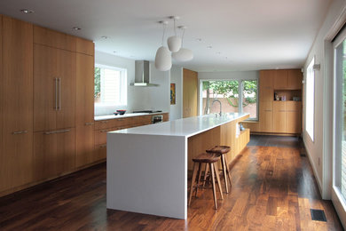 Inspiration for a large modern galley dark wood floor kitchen remodel in New York with an integrated sink, flat-panel cabinets, medium tone wood cabinets, solid surface countertops, white backsplash, ceramic backsplash, paneled appliances and an island