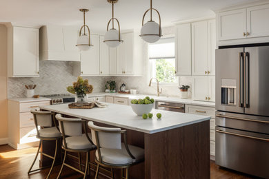 Example of a transitional l-shaped medium tone wood floor and brown floor kitchen design in DC Metro with a farmhouse sink, shaker cabinets, white cabinets, white backsplash, stainless steel appliances, an island and white countertops