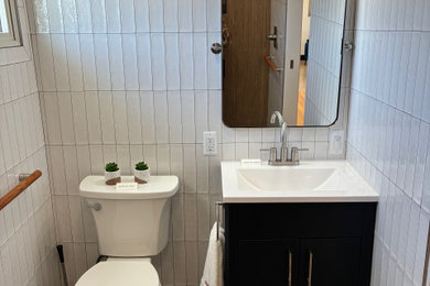 Inspiration for a mid-sized 1950s white tile and porcelain tile pebble tile floor, gray floor and single-sink bathroom remodel in Other with shaker cabinets, black cabinets, a two-piece toilet, white walls, an integrated sink, white countertops and a freestanding vanity