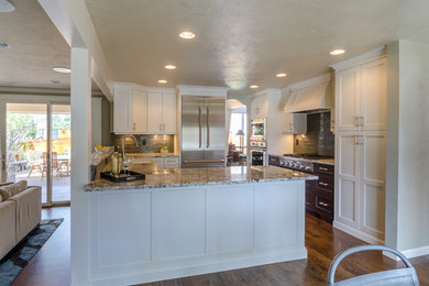 Inspiration for a mid-sized transitional u-shaped medium tone wood floor eat-in kitchen remodel in Denver with a farmhouse sink, shaker cabinets, white cabinets, green backsplash, glass tile backsplash, stainless steel appliances and a peninsula